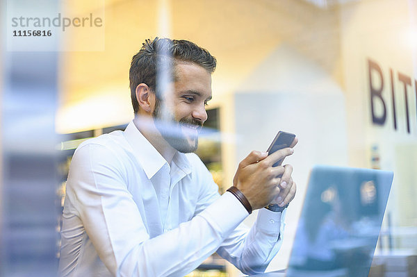 Lächelnder Geschäftsmann beim Anblick eines Handys in einem Café