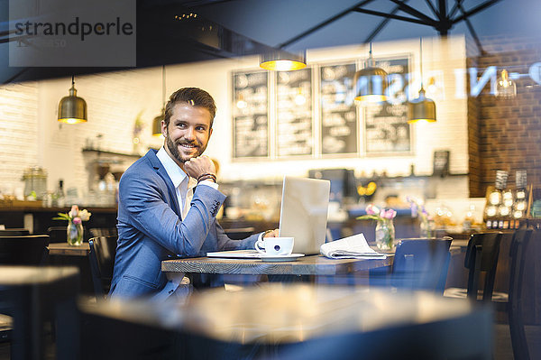 Lächelnder Geschäftsmann mit Laptop im Cafe