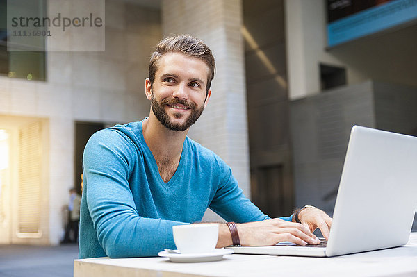 Lächelnder junger Mann am Tisch sitzend mit Laptop