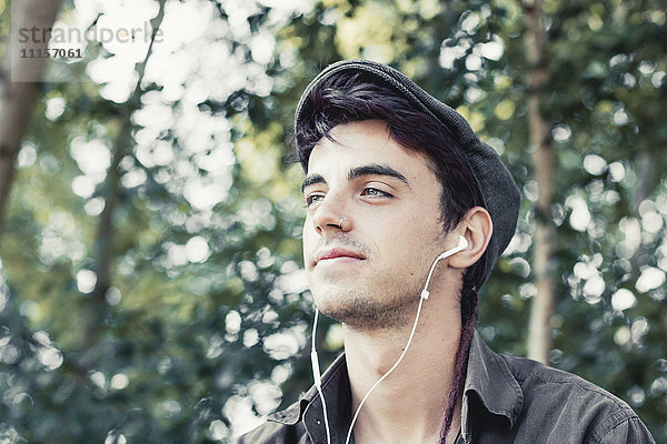 Porträt eines lächelnden jungen Mannes mit Mütze  der Musik mit Kopfhörern hört.