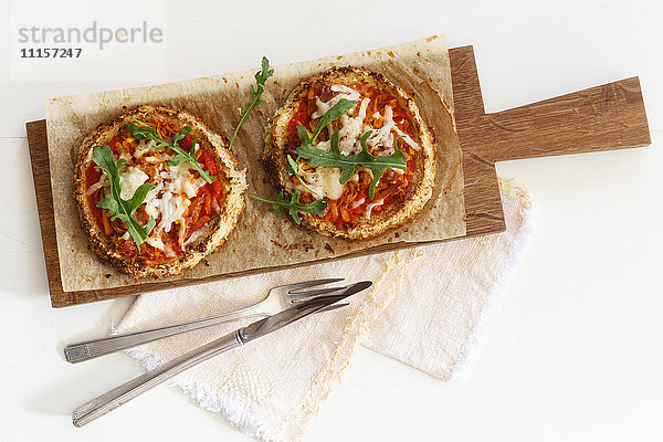 Zwei hausgemachte glutenfreie Mini-Pizzen mit Blumenkohl  Kürbis und Rucola auf Holzplatte
