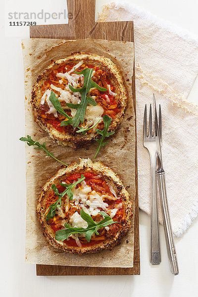Zwei hausgemachte glutenfreie Mini-Pizzen mit Blumenkohl  Kürbis und Rucola auf Holzplatte