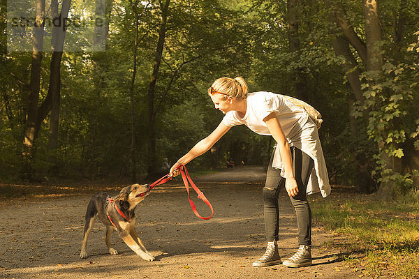 Junge Frau spielt mit ihrem Hund auf einem Waldweg