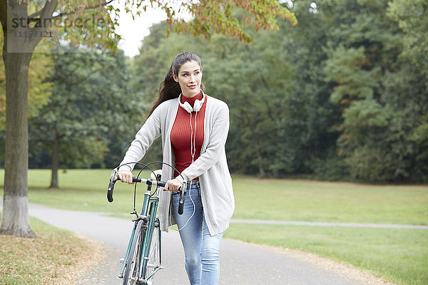 Frau mit Kopfhörer und Fahrrad im Herbstpark