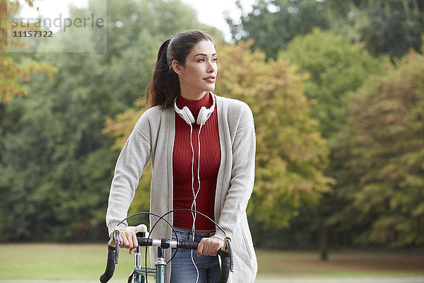 Frau mit Kopfhörer und Fahrrad im Herbstpark