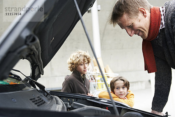 Vater schaut sich ein kaputtes Auto an  während die Kinder warten.