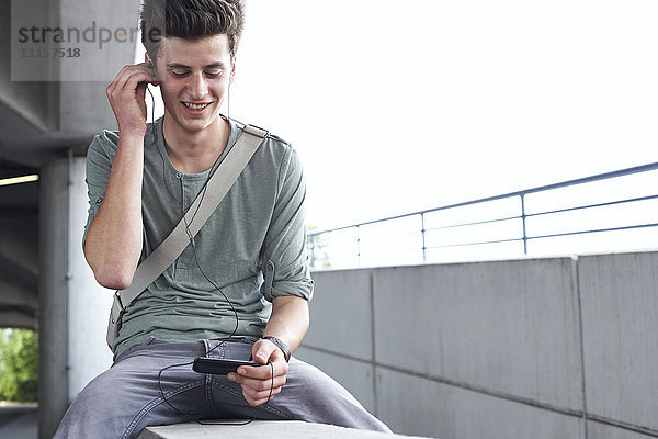 Lächelnder Teenager mit Handy und Ohrhörern im Freien