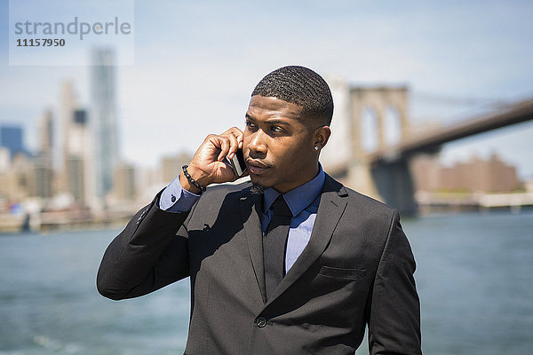 USA  Brooklyn  Porträt eines Geschäftsmannes am Telefon vor der Skyline von Manhattan