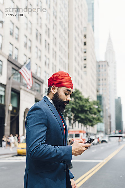 Indischer Geschäftsmann beim Überqueren der Straße in Manhattan  Blick auf Smartphone