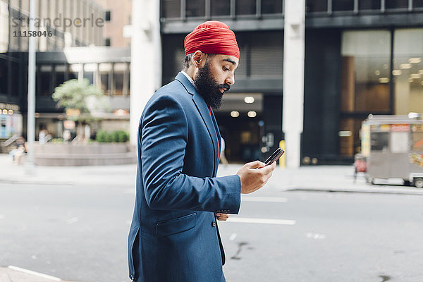 Indischer Geschäftsmann in Manhattan mit Smartphone  zu Fuß auf der Straße