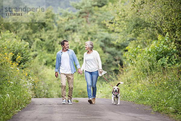 Glückliches Seniorenpaar auf einem Spaziergang mit Hund in der Natur