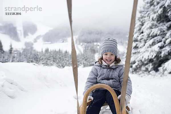 Glückliches Mädchen auf Schlitten in der Winterlandschaft