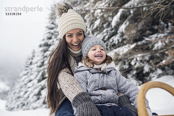 Glückliche Mutter mit Tochter auf Schlitten in Winterlandschaft