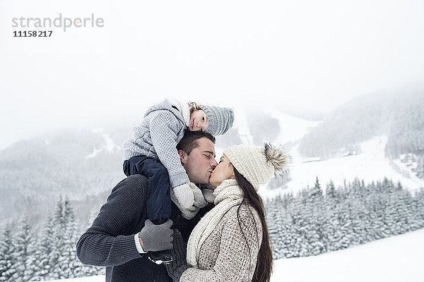 Paar mit Tochter beim Küssen in der Winterlandschaft