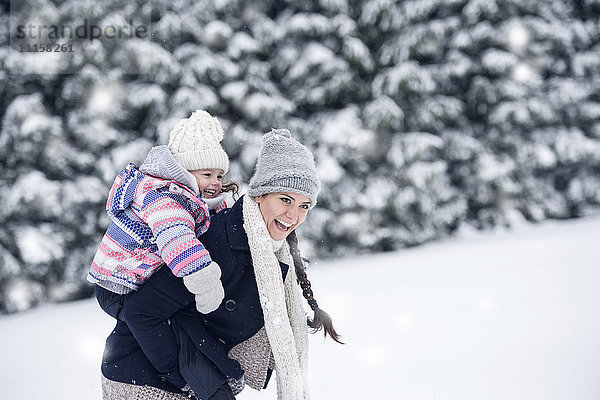 Glückliche Mutter mit Tochter Huckepack in Winterlandschaft