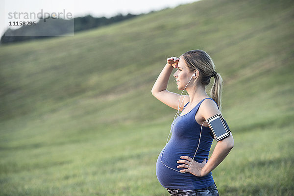 Schwangere Frau  die auf dem Feld steht und eine Pause vom Joggen macht