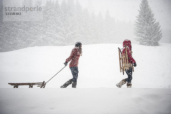 Zwei junge Frauen mit Schlitten bei starkem Schneefall