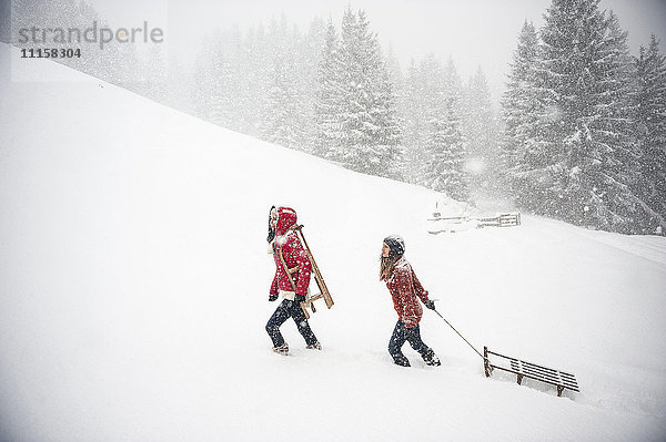 Zwei junge Frauen mit Schlitten bei starkem Schneefall