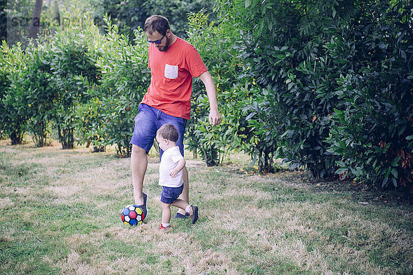 Vater spielt Fußball mit seinem kleinen Sohn auf einer Wiese