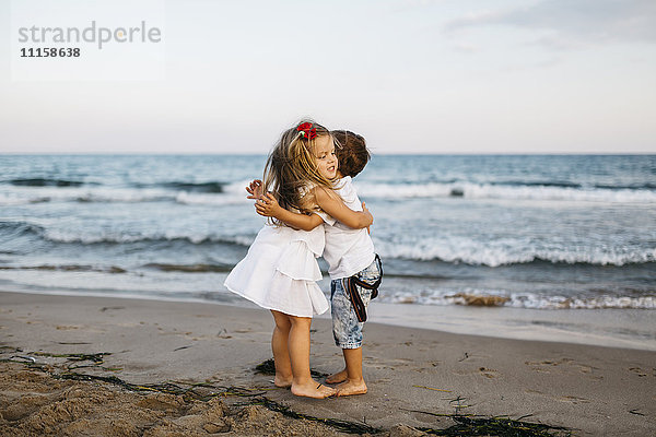 Kleines Mädchen umarmt kleinen Jungen am Strand