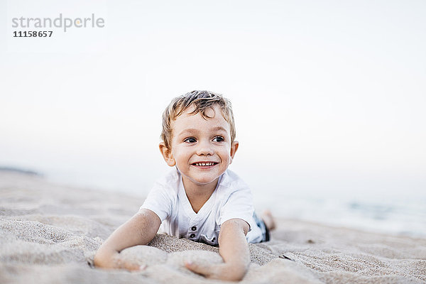 Porträt eines glücklichen kleinen Jungen  der am Strand liegt.