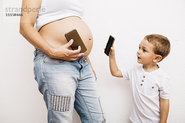 Schwangere Mutter und kleiner Sohn beim Spielen mit Smartphones