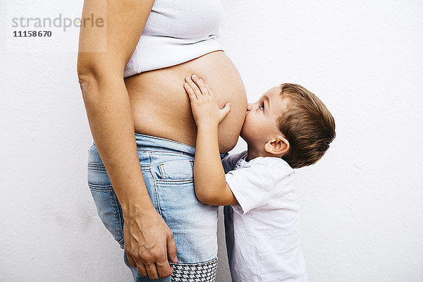 Kleiner Junge  der den Bauch einer schwangeren Mutter küsst.