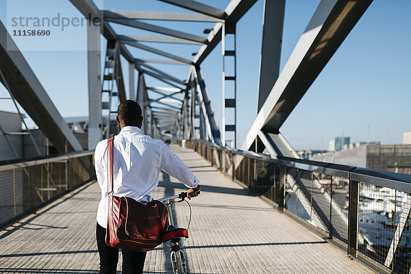 Mann schiebt Fahrrad auf einer Brücke