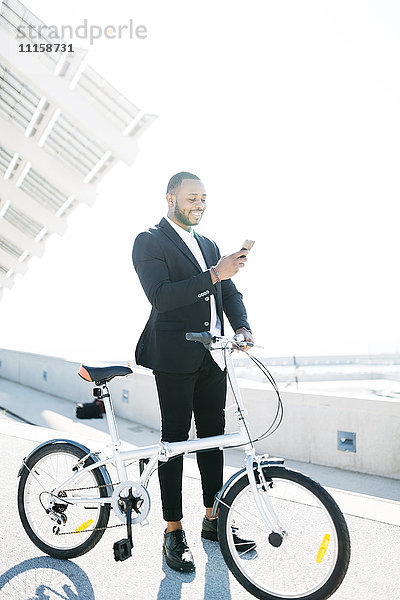 Lächelnder Geschäftsmann mit Fahrrad beim Blick aufs Handy