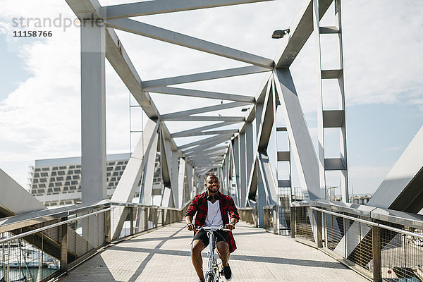 Lächelnder Mann beim Fahrradfahren auf einer Brücke