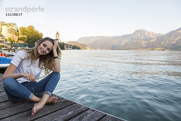 Österreich  Sankt Wolfgang  lächelnde Frau sitzt am Steg am See