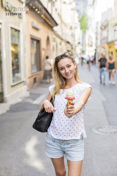 Österreich  Salzburg  Frau auf der Einkaufsstraße  die dem Zuschauer ihre Eistüte anbietet.
