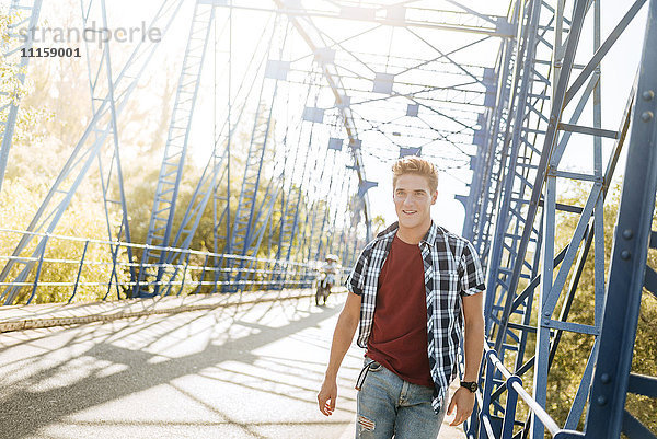 Lächelnder junger Mann  der auf einer Brücke geht.
