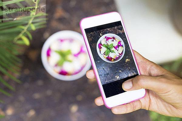 Frau fotografiert tropischen Obstsalat mit Handy  Nahaufnahme