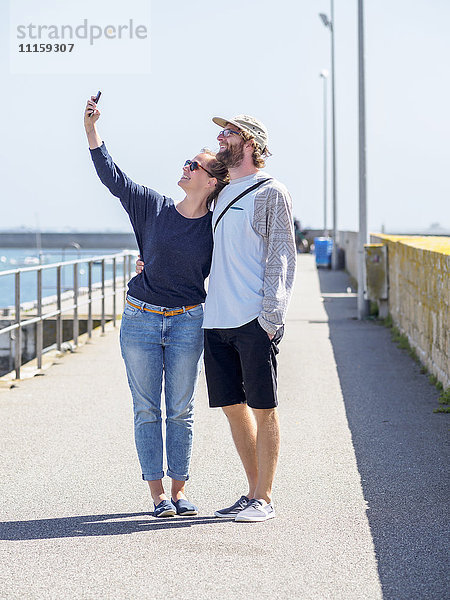 Frankreich  Bretagne  Finistere  glückliches junges Paar  das sich mit einem Smartphone im Hafen vergnügt.
