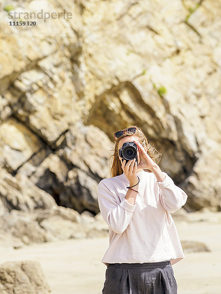 Frau steht am Strand und macht ein Foto mit der Kamera.