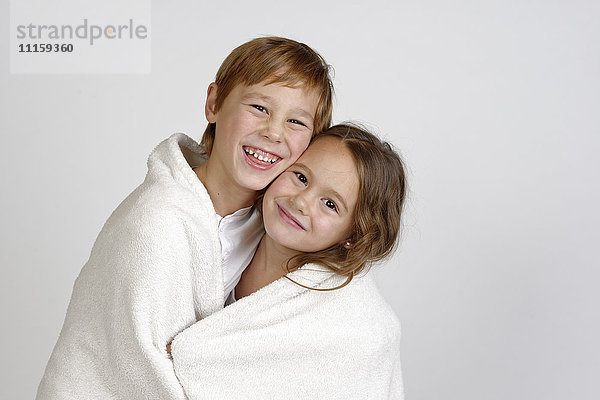 Porträt eines lachenden Jungen  der mit seiner kleinen Schwester eine Decke teilt.