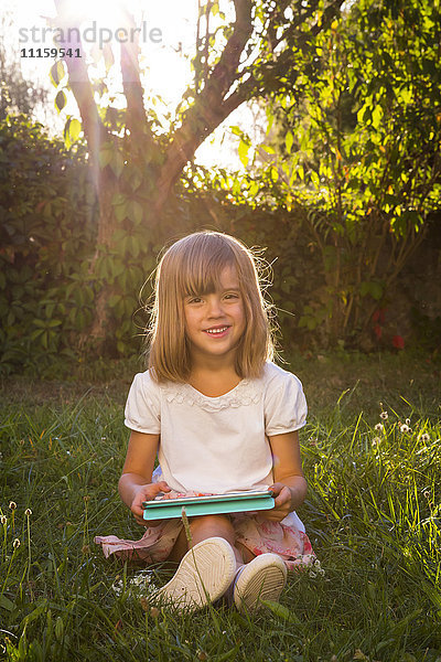 Porträt eines lächelnden Mädchens auf einer Wiese mit Tablette