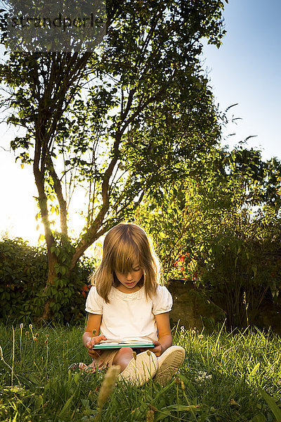 Kleines Mädchen sitzend auf einer Wiese mit Tablette