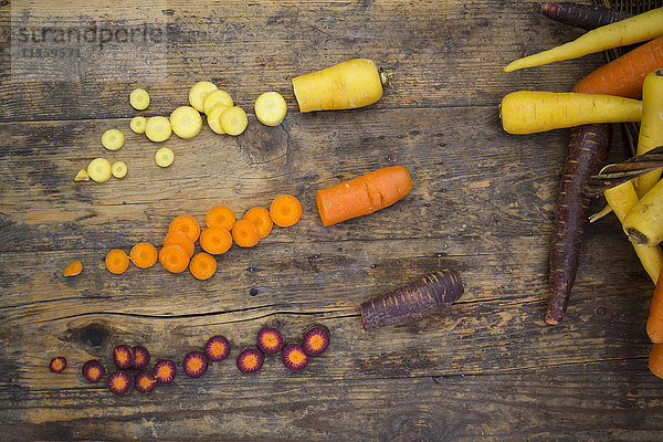 Drei verschiedene Arten von ganzen und geschnittenen Karotten auf Holz
