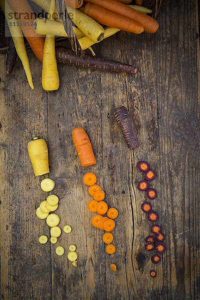 Drei verschiedene Arten von ganzen und geschnittenen Karotten auf Holz