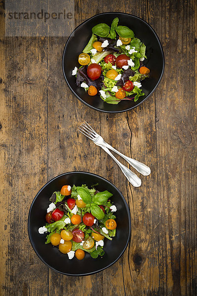 Zwei Schalen Blattsalat mit Ziegenfrischkäse und Tomaten auf Holz