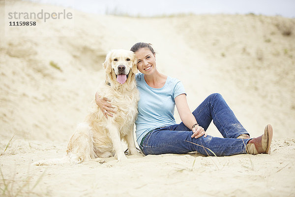 Lächelnde junge Frau mit Hund im Sand