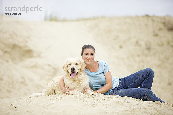 Lächelnde junge Frau mit Hund im Sand