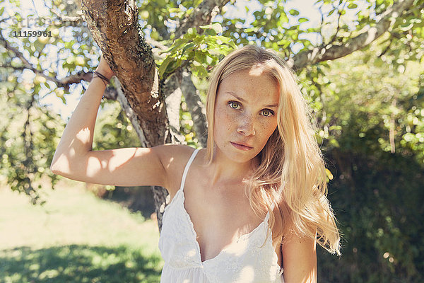 Porträt einer jungen blonden Frau am Apfelbaum