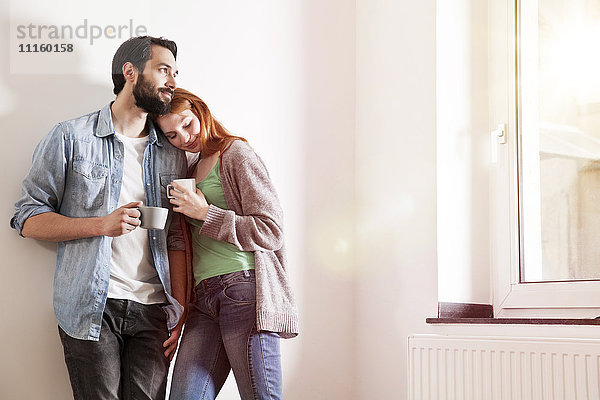 Lächelndes junges Paar mit Tassen in der Wohnung