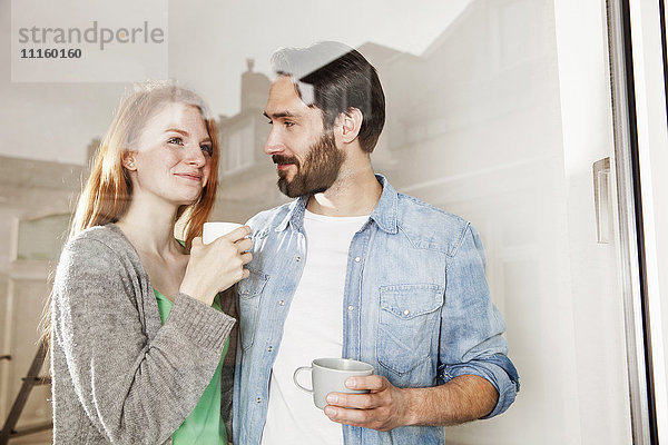 Lächelndes junges Paar bei einer Kaffeepause hinter der Fensterscheibe