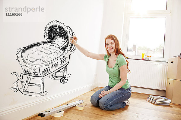 Junge Frau beim Zeichnen eines Babybettes an der Wand in der neuen Wohnung