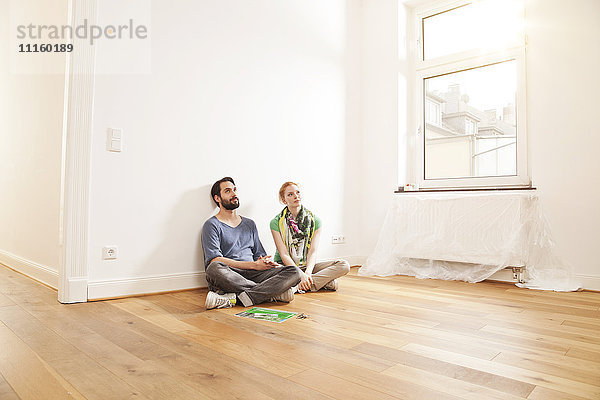 Junges Paar auf dem Boden sitzend in einer leeren Wohnung