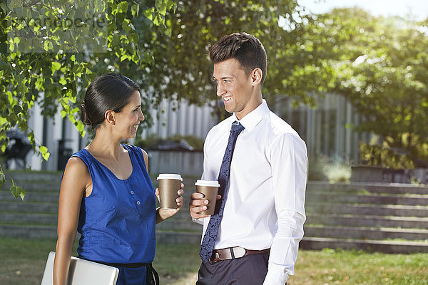 Lächelnde Geschäftsfrau und Geschäftsmann mit Kaffee zum Mitnehmen im Freien